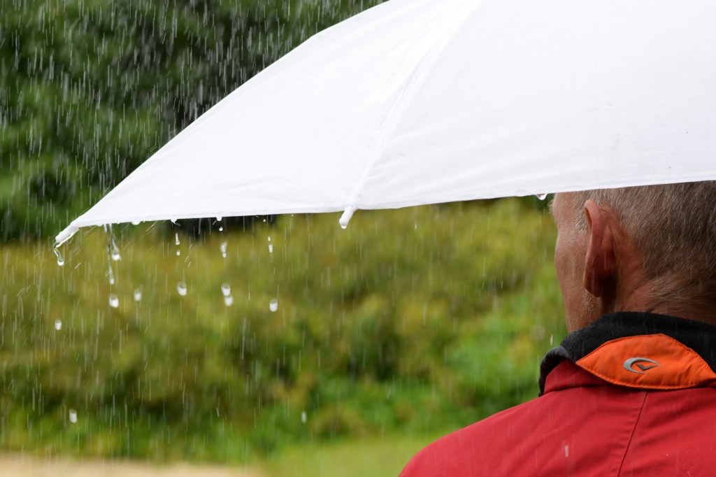 A man stands in the rain holding a white umbrella.